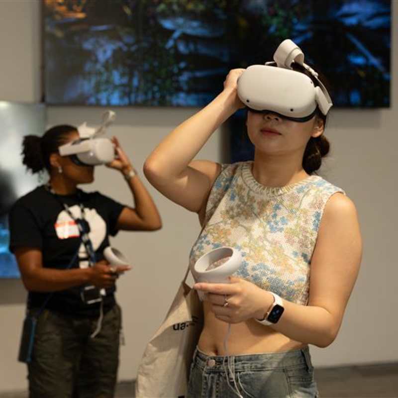 Two students standing in the gallery with headsets. 