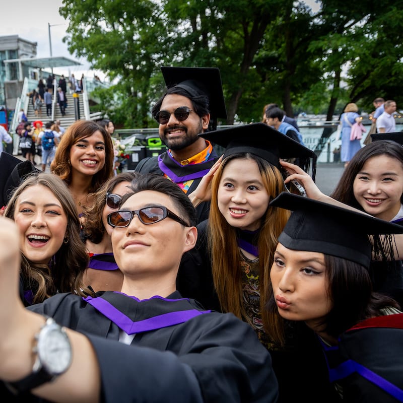 A group of graduating UAL students wearing hats a robes taking a selfie.