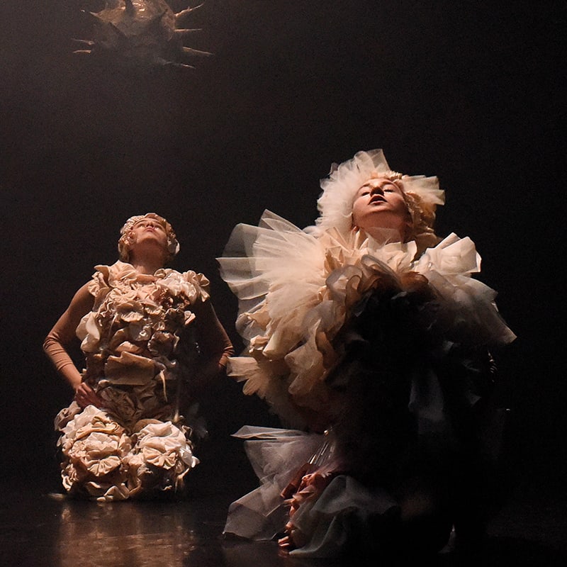 Two women in costumes kneeling on a stage