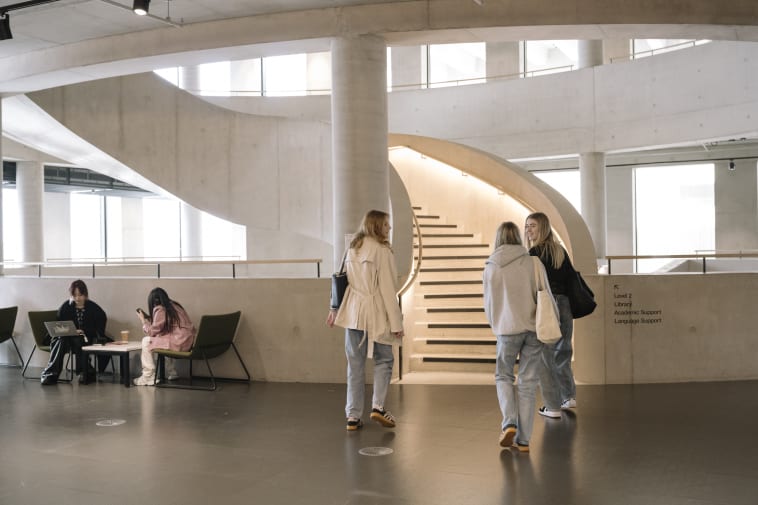 Three people with their backs to the camera walking towards a staircase and talking to each other.