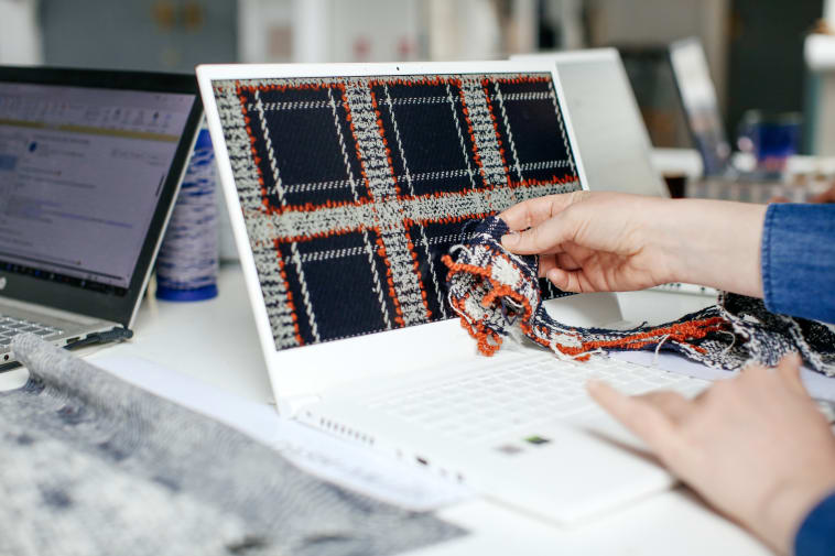 A photo of someone holding some colorful fabric up to a laptop.