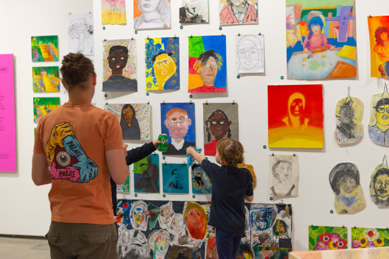 An adult and child in front of a wall of different portrait styles