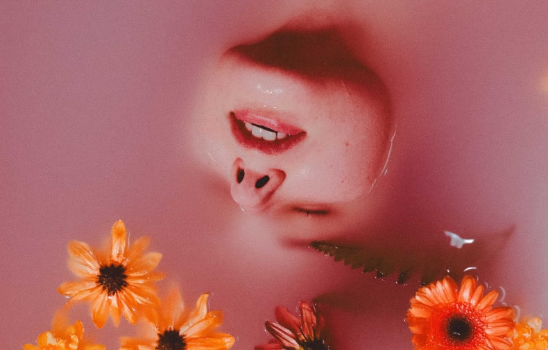 A woman lying in a pink bath with flowers