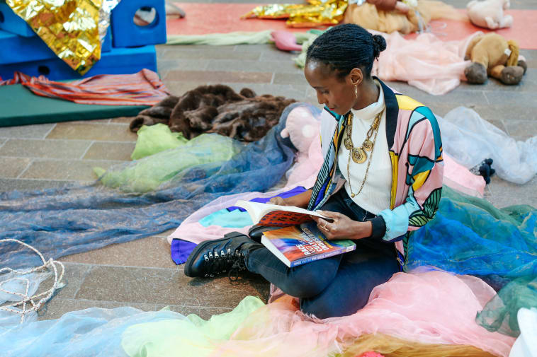 A stuent sat on the floor surrounded by various coloured textiles