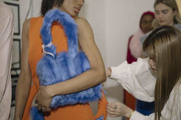 Student making finishing touches on model's outfit.