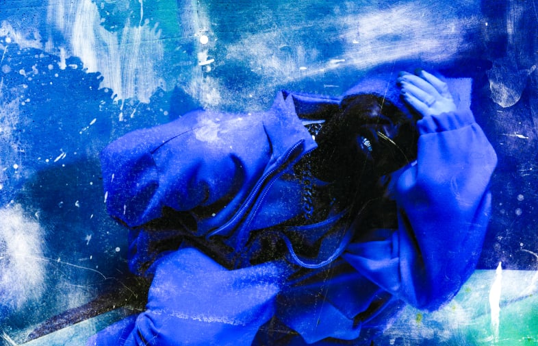 Model crouched down in blue tracksuit and a blue and green tint to the image with textured marks overlaying.