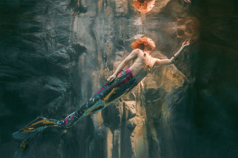 Photograph of an orange haired model underwater, swimming towards the light