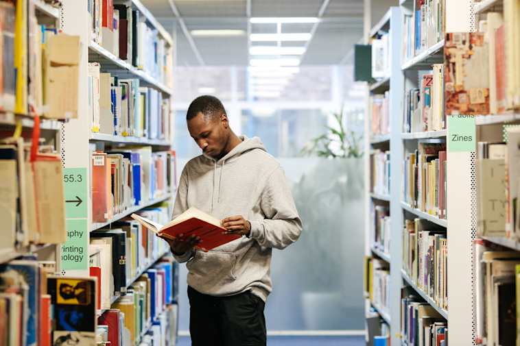 Student browsing a book from library shelves