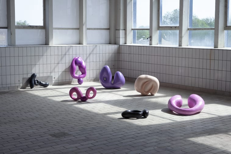 A selection of pink and purple coloured sculptures positioned on a white tiled area