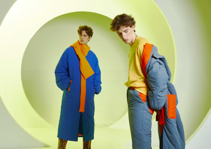 2 males wearing blue outerwear stood infront of green background