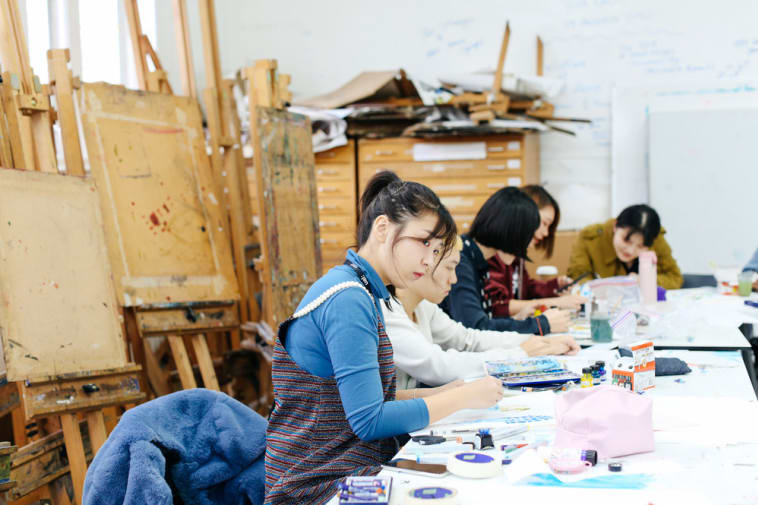 Students painting in a studio surrounded by easels.