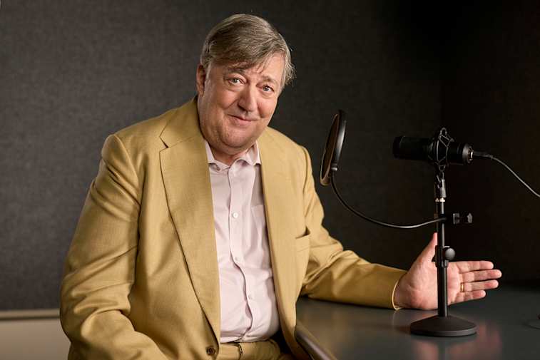 An image of a man at a table resting his hand on a microphone
