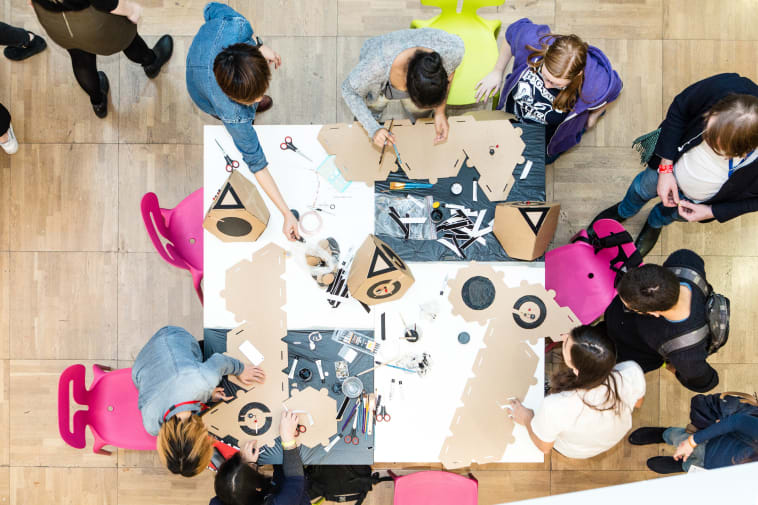 a group of students sit round a table, they are making models out of cardboard boxes