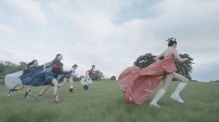 Students running in an open field wearing big dresses.
