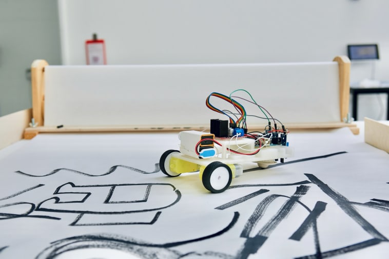 Photo of a small battery powered robot following black lines on a large roll of paper