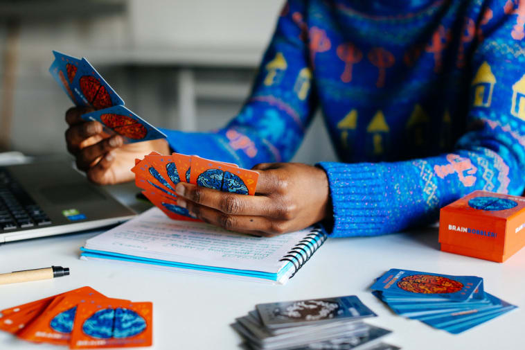 Hands in a blue and orange pattern jumper, holding up orange and blue cards with an image of a brain drawn on the back.