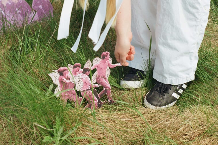 A mixed-media collage featuring 4 men with fairy wings running in the grass
