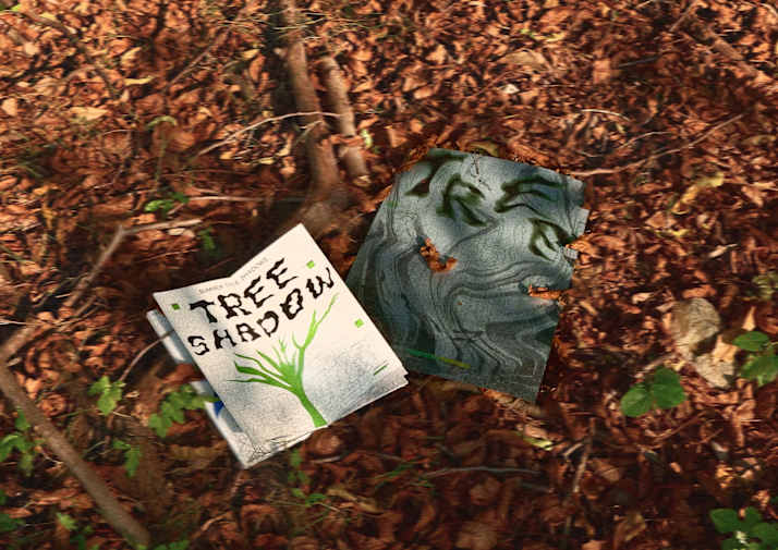 A student publication titled Tree Shadow placed on a forest floor covered in dry leaves, alongside a second printed piece with abstract green and grey imagery inspired by tree shadows.