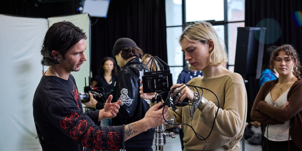 A group of people is engaged in a film or photography setup, adjusting camera equipment in a studio setting.