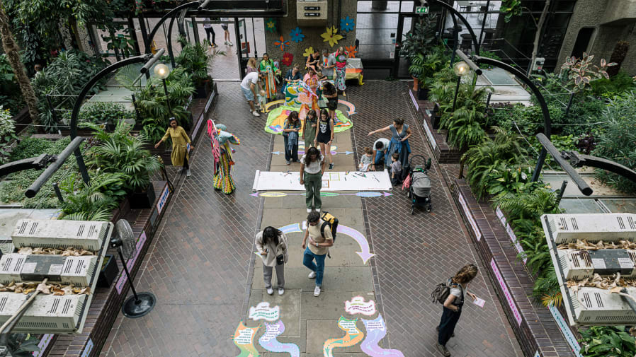 People walk along a path with information written on the floor. Plants line the path either side