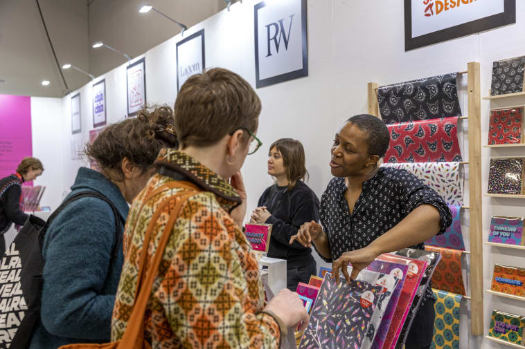  People at a booth in a trade show discussing colorful patterned products displayed on shelves