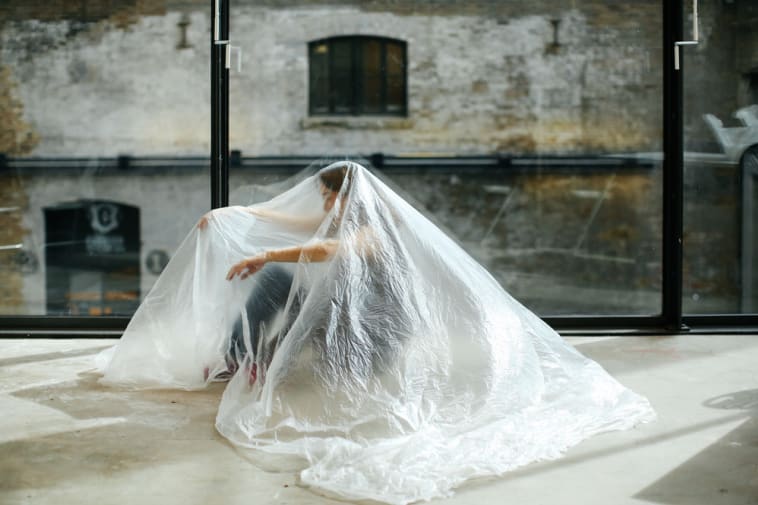 Person in an empty room with a plastic sheet draped over them