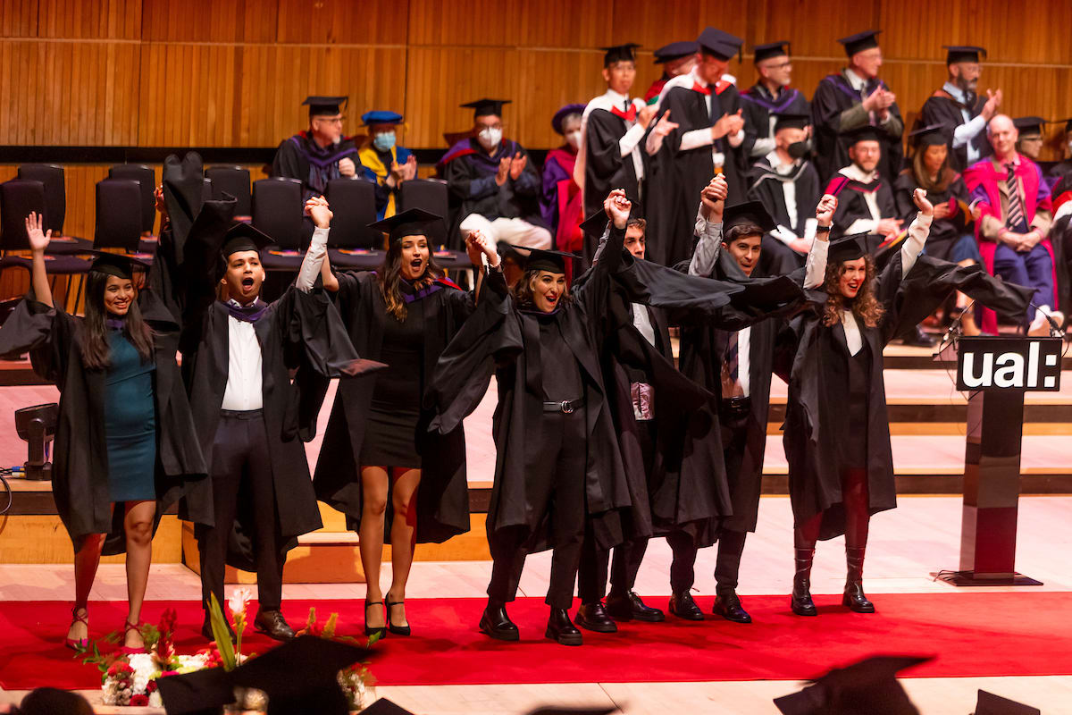Queue of people wearing academic gowns, some holding arms aloft in celebration