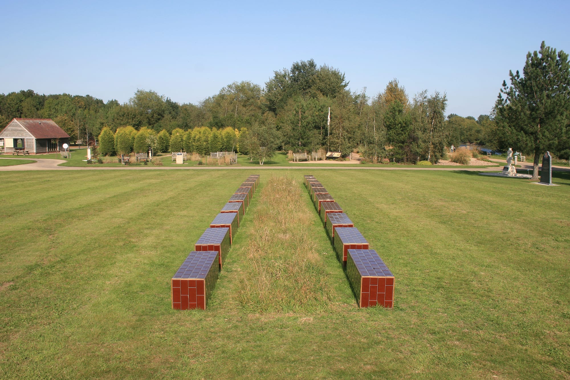 Benches made in brown tiling set in green space with plants and flowers growing in between