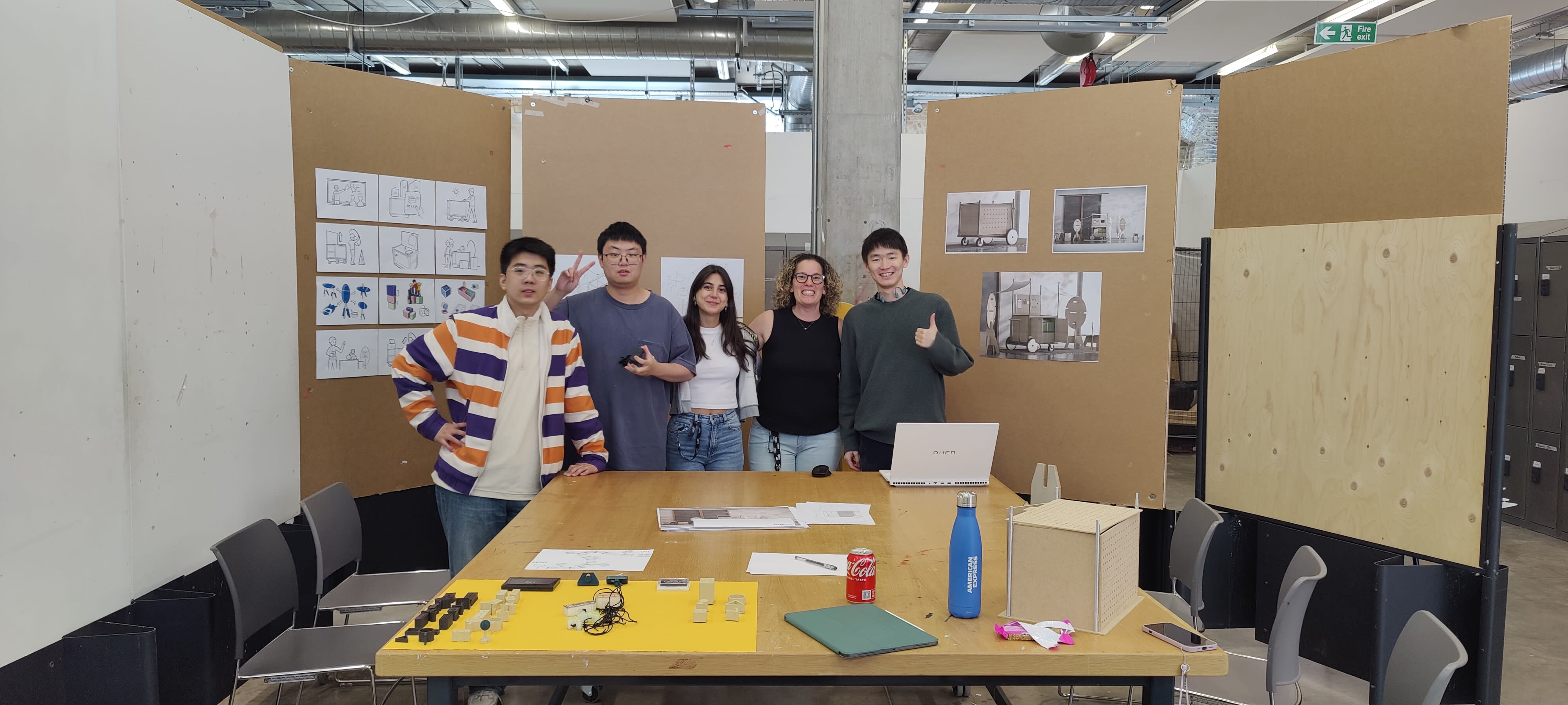 Five students stood in a classroom with a desk and chairs.