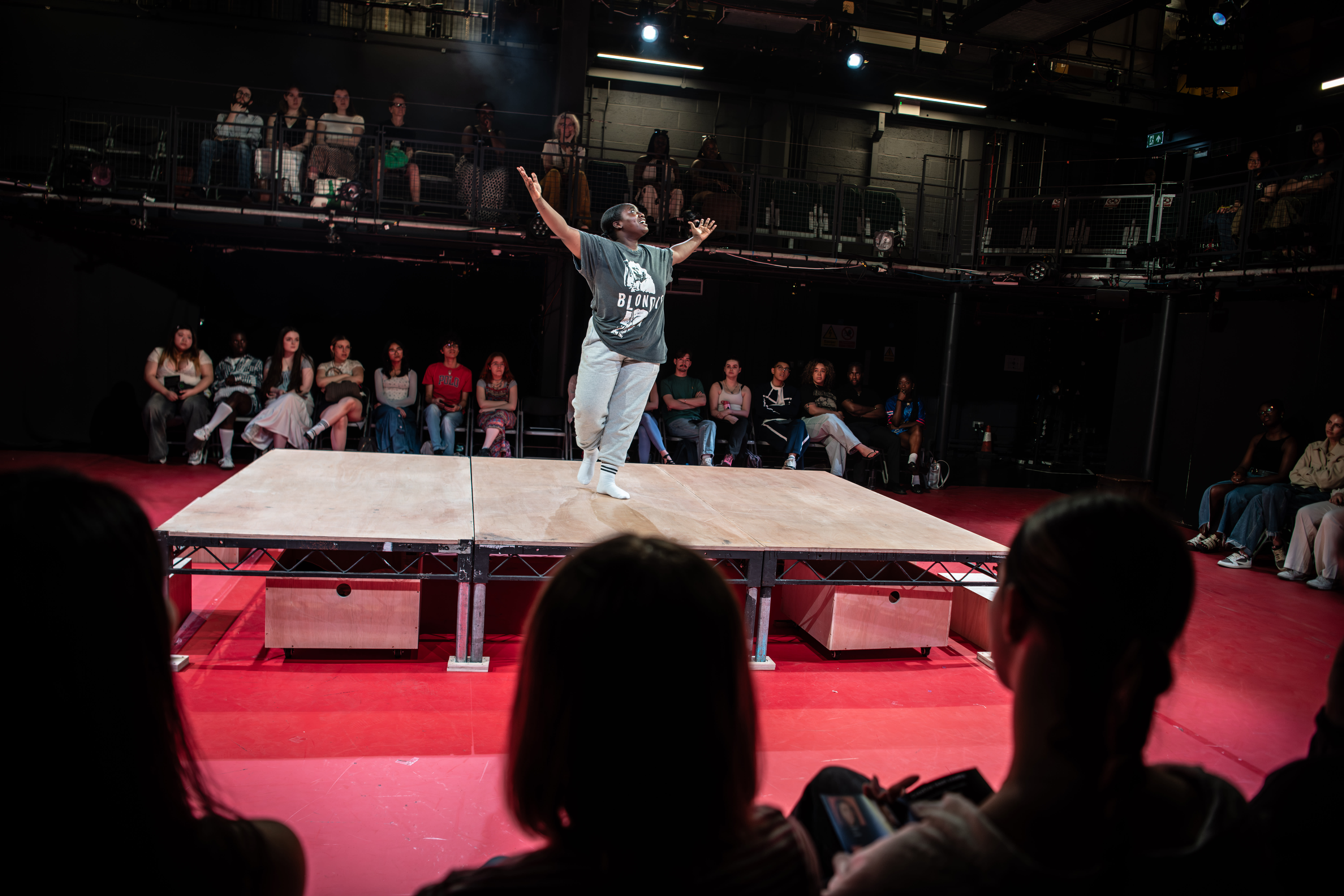 A performer dances passionately on stage, surrounded by an engaged audience seated in a theater with a vibrant red floor.