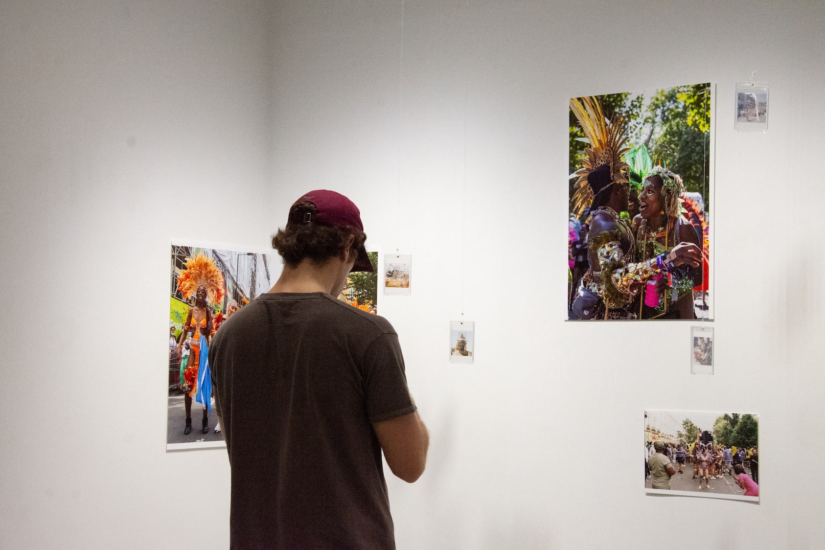 A person in a baseball cap with back to camera is in front of 3 photographic works showing Notting Hill Carnival