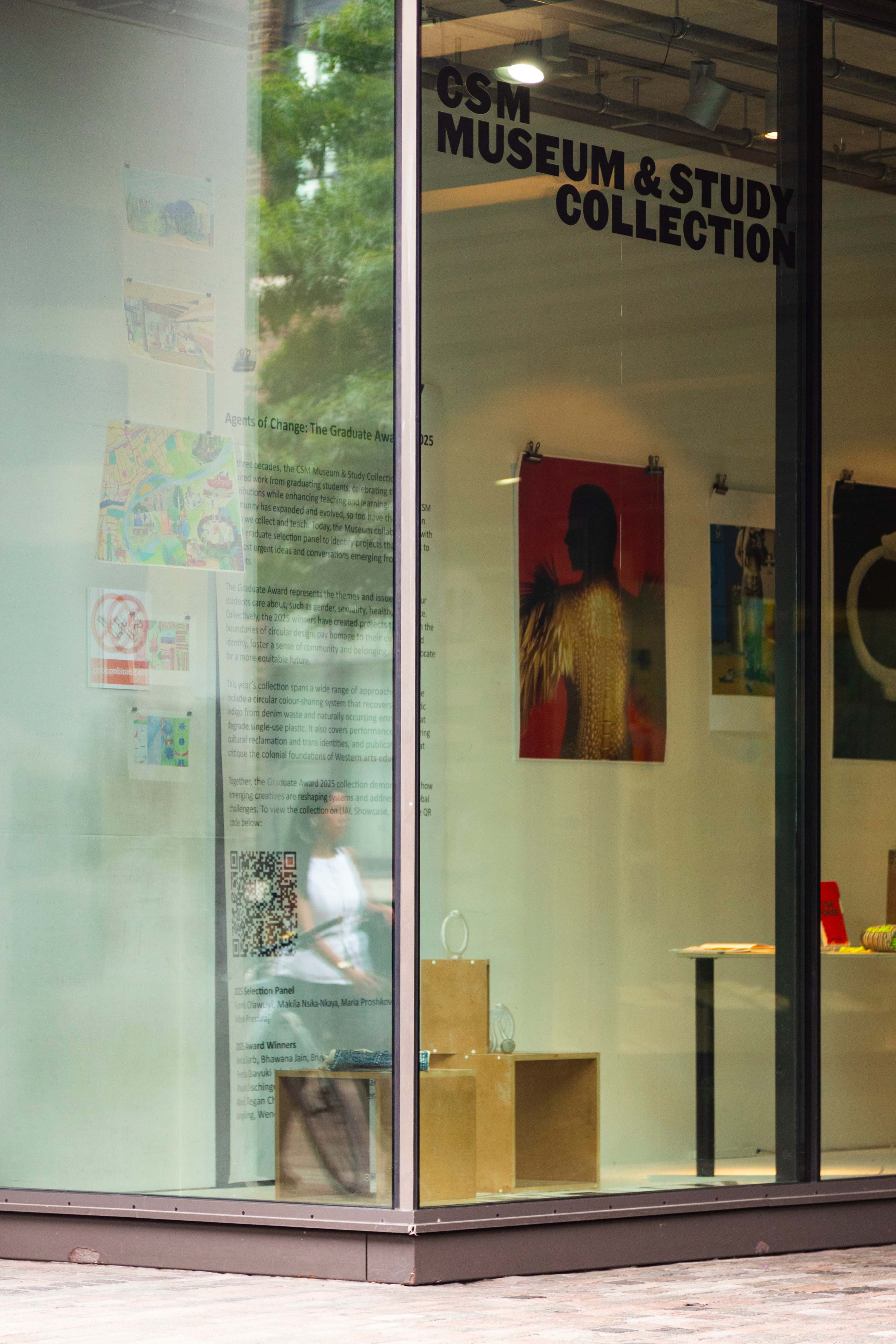 A side shot of the Museum window with the installation in place. A person is walking past and we see their slightly blurred reflection.