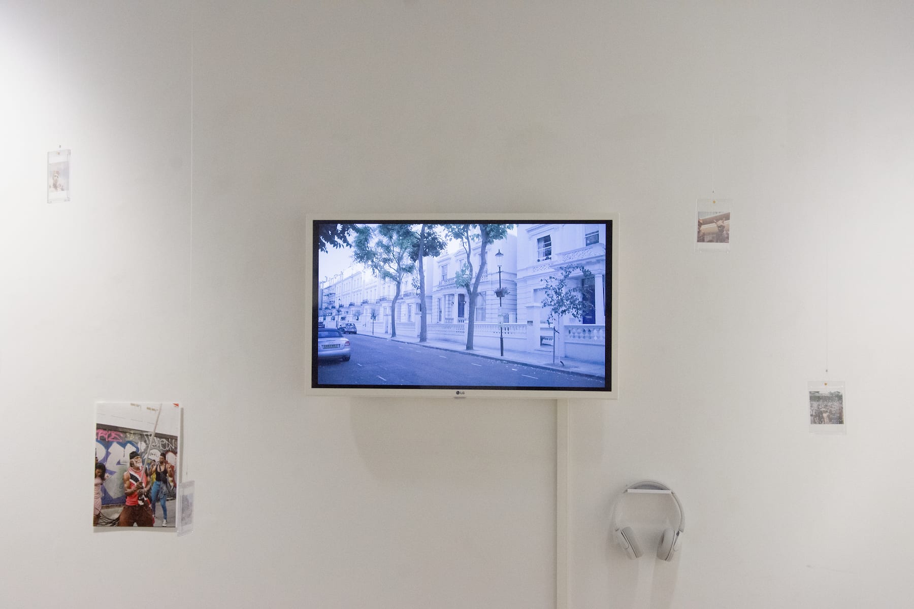 A hanging screen with a bluescale scene from a recognisably West London street with a row of storeyed houses and railings all painted white. There are other smaller artworks at either side and a hanging set of white earphones 