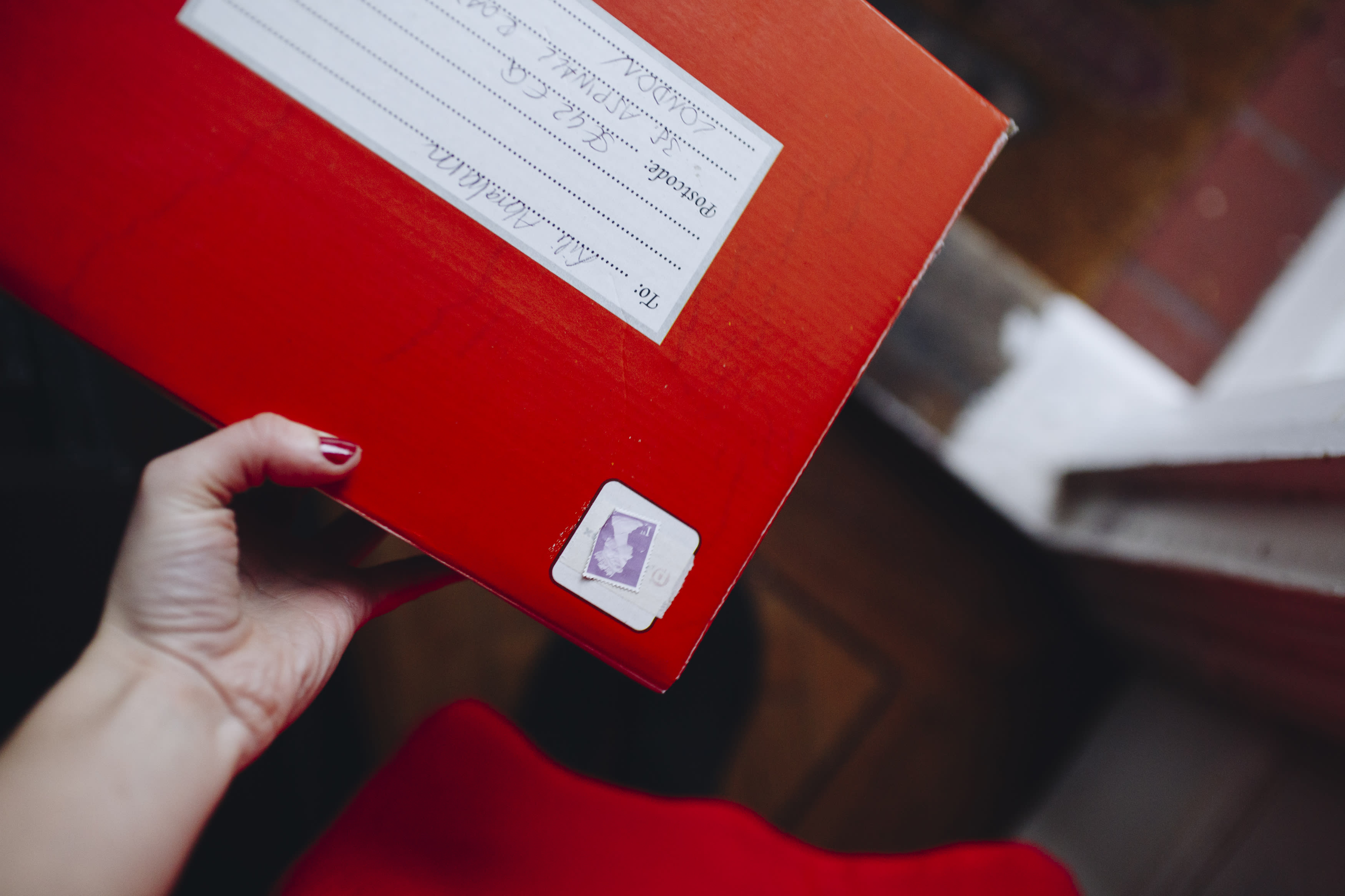 A hand holding a red Royal Mail package.