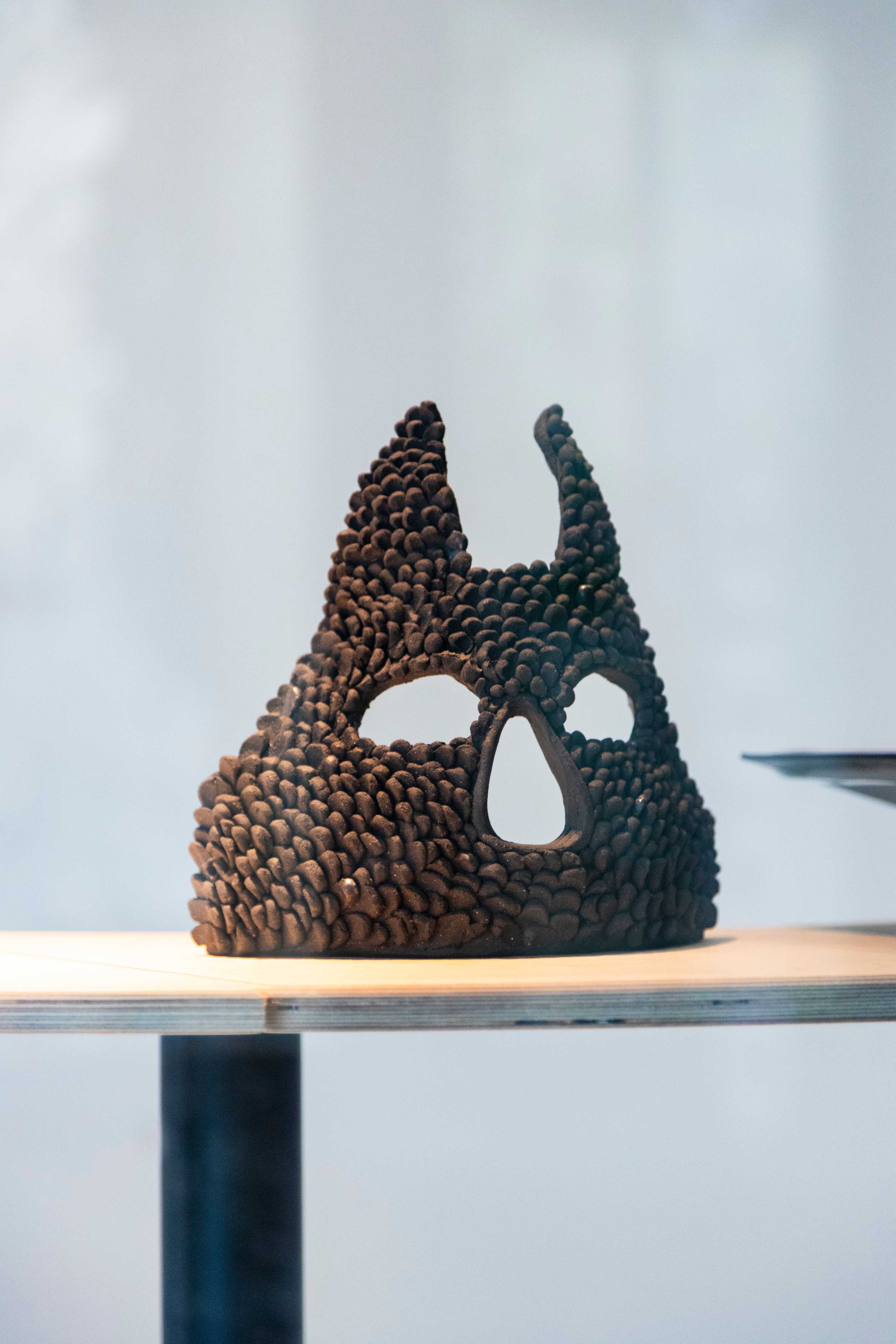 A slightly curved mask-like sculpture of an animal face is placed upright on a tabletop.