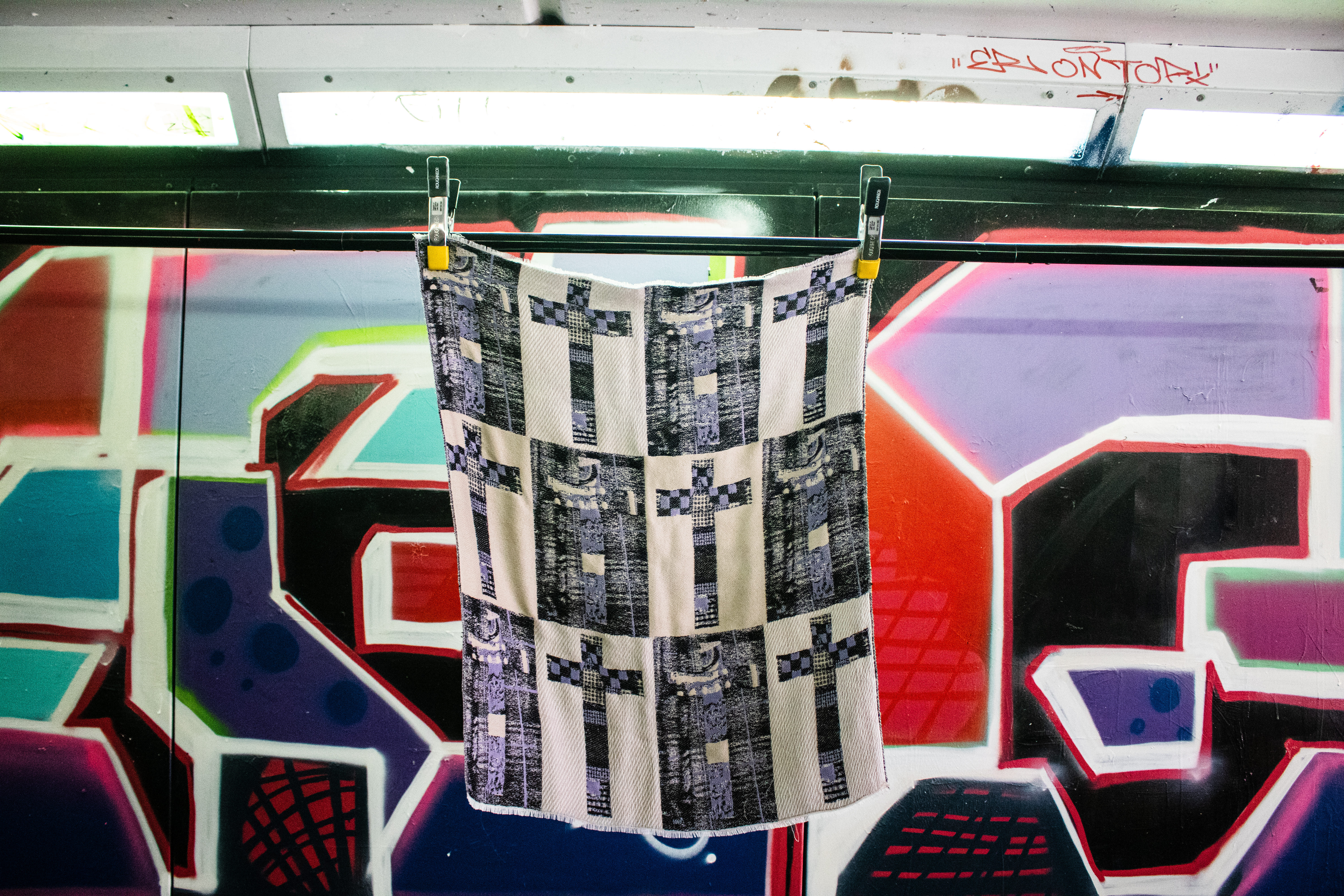 Purple, black and white quilt with crosses hung up against a colourful background.