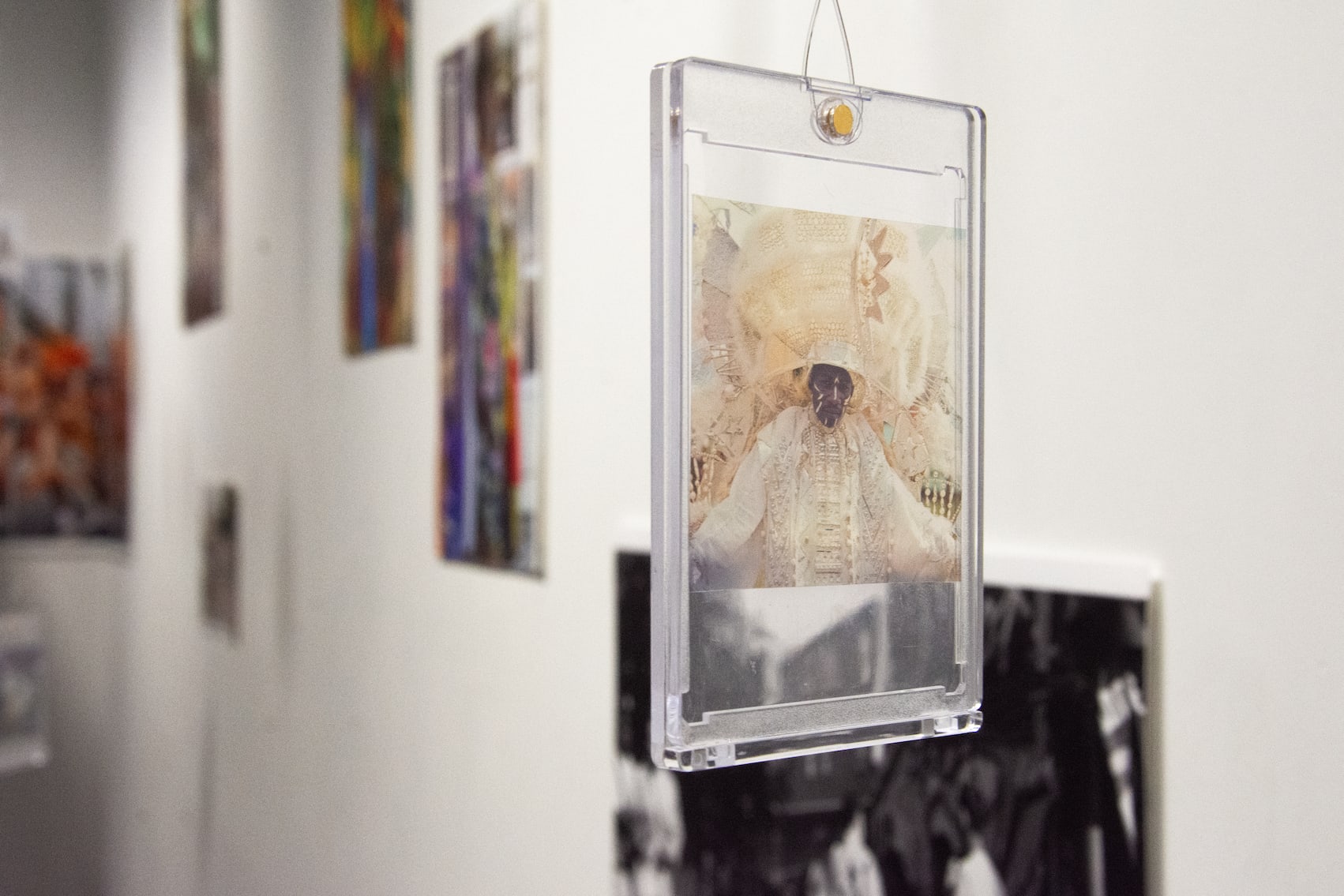 Close-up of a hanging photograph of a person in ornate white carnival dress inside a small perspex frame