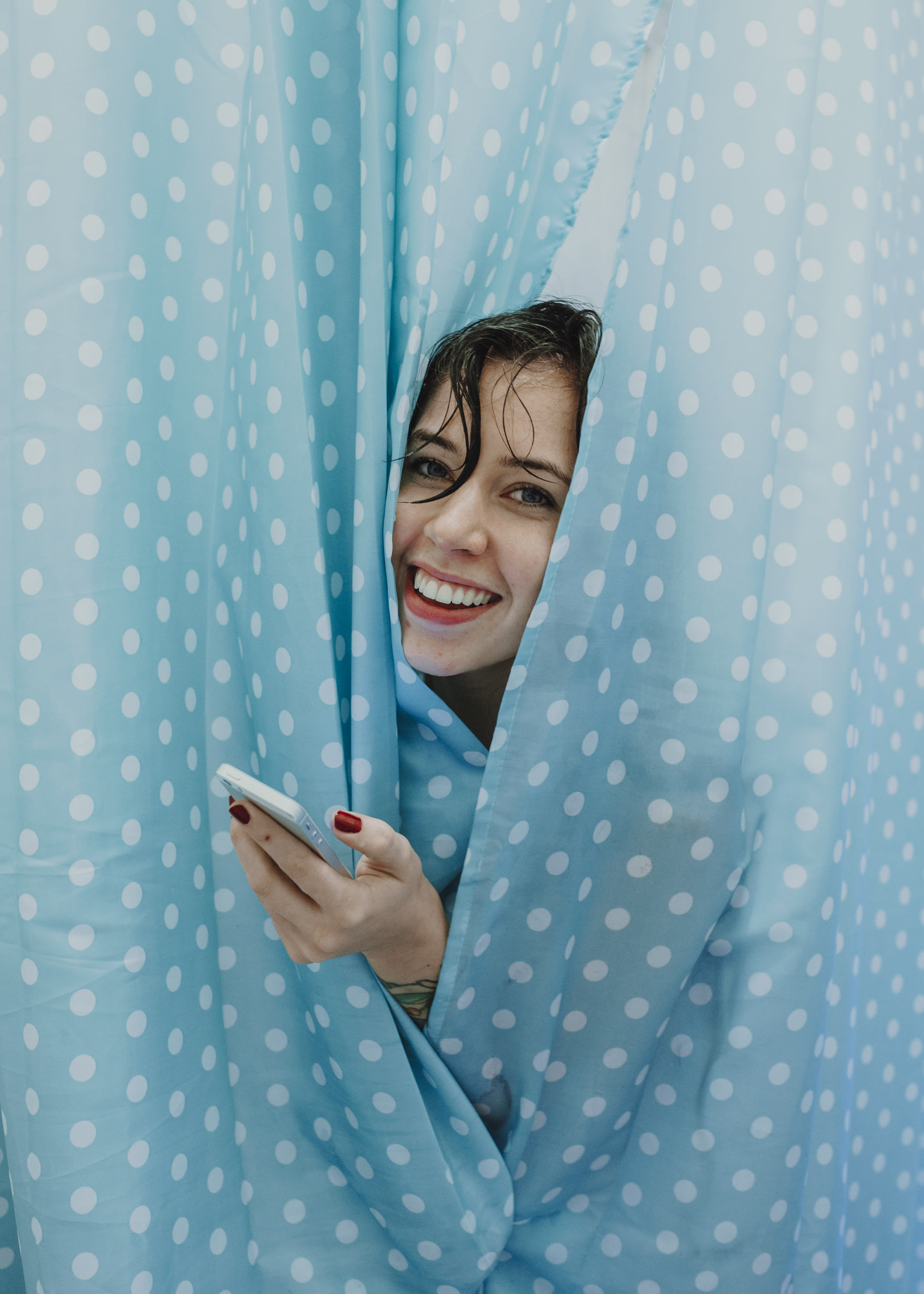 A person peeping out of blue shower curtains.