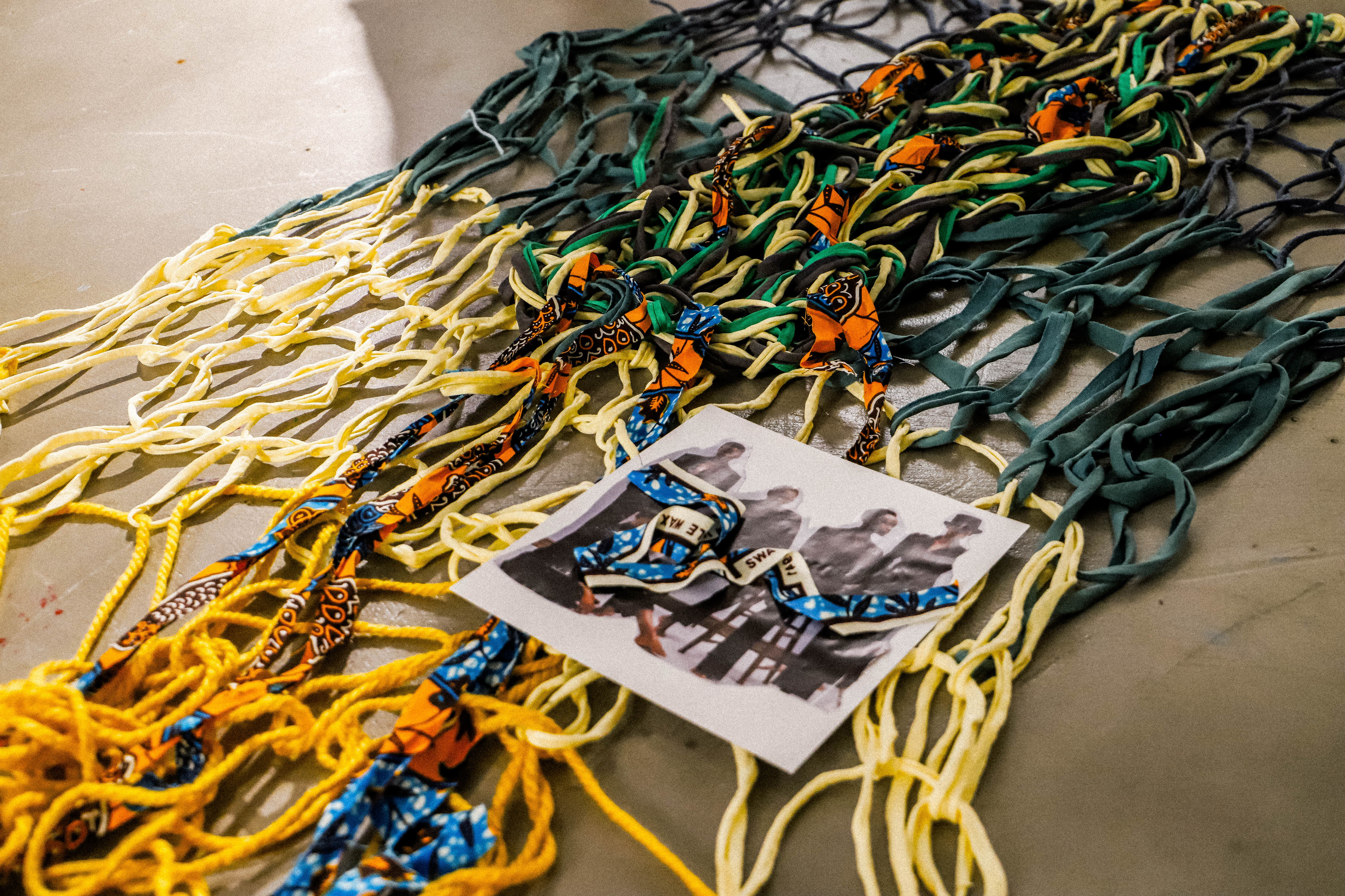 Colorful yellow, green, black, and orange cords form a tangled net, with a small photo and blue-orange lanyards layered on top.