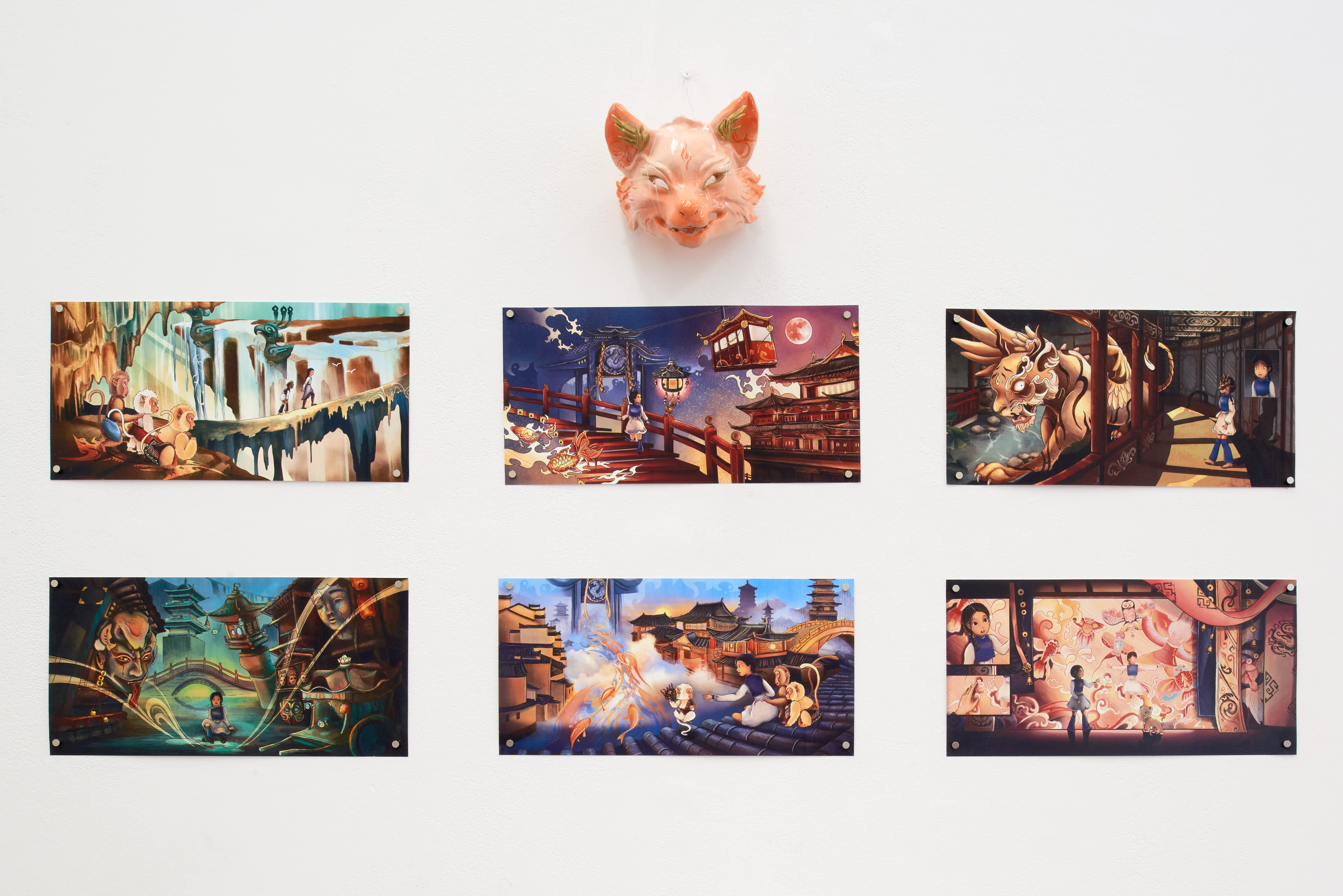 Six colourful fantasy illustrations displayed on a white wall beneath a sculpted animal head, depicting figures, creatures and East Asian-inspired architecture.