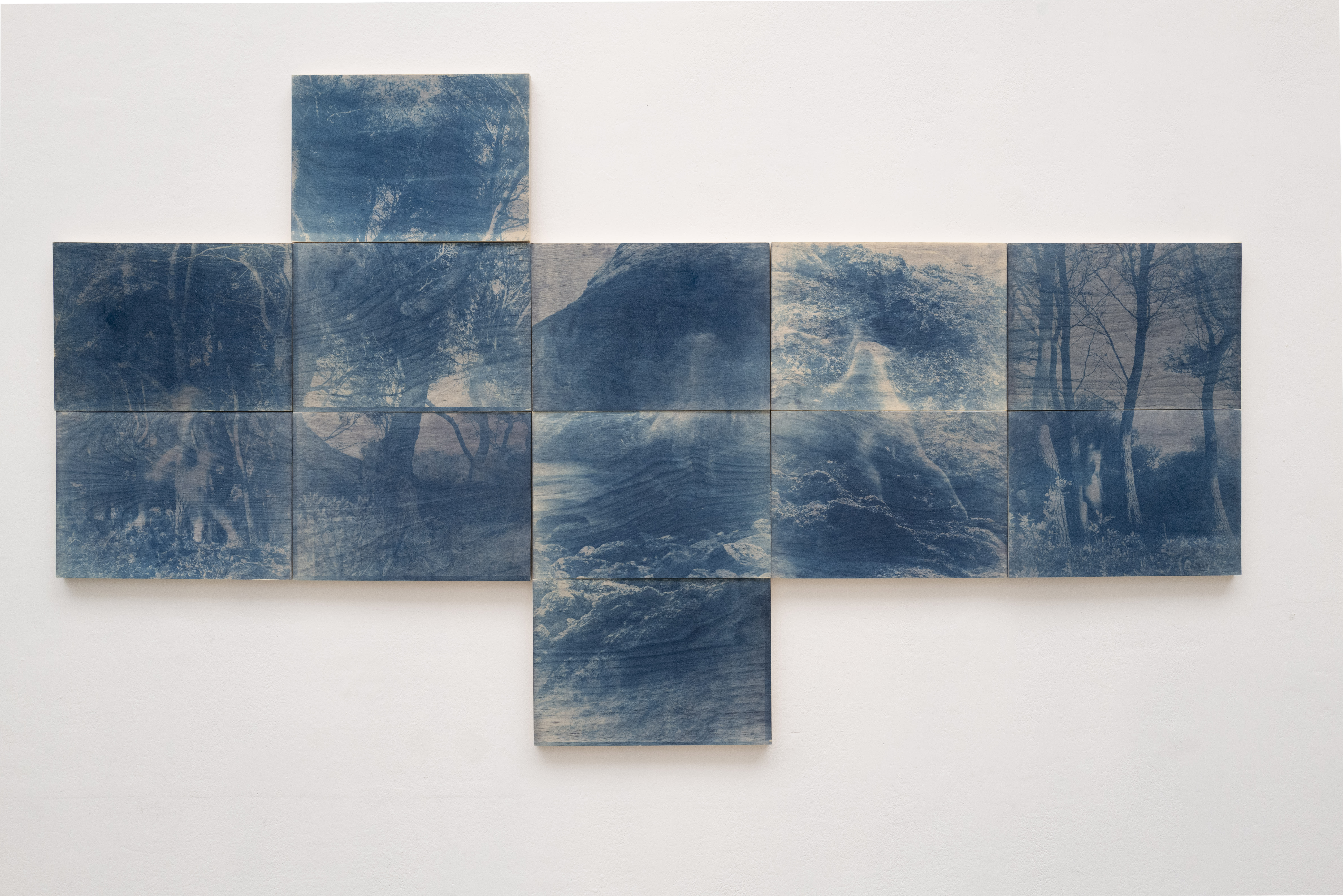 Wall view of a photography piece showing multiple panels arranged in a asymmetrical configuration. Blue photographs are featured on the surface.