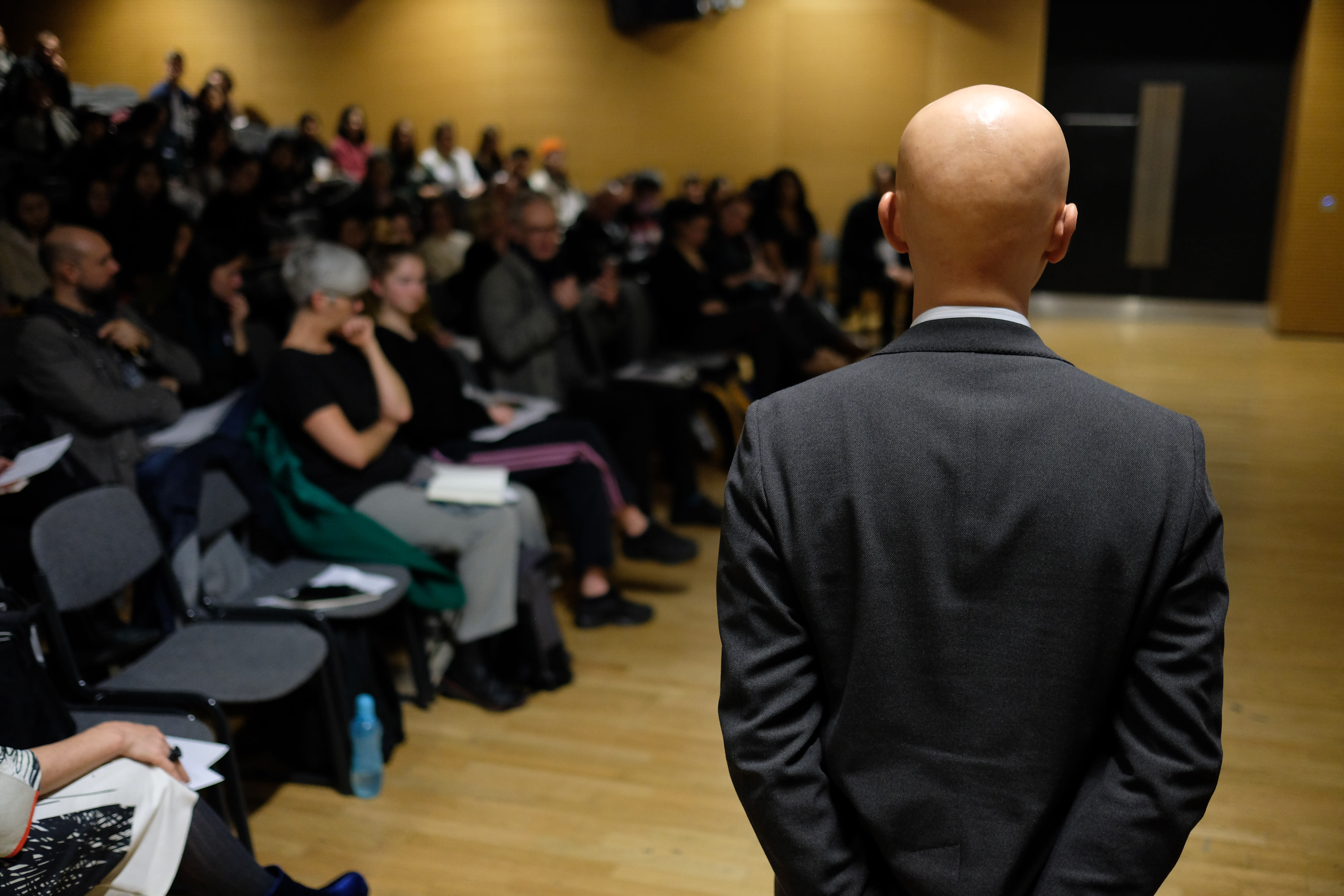 A man in a suit seen from behind in a lecture theatre
