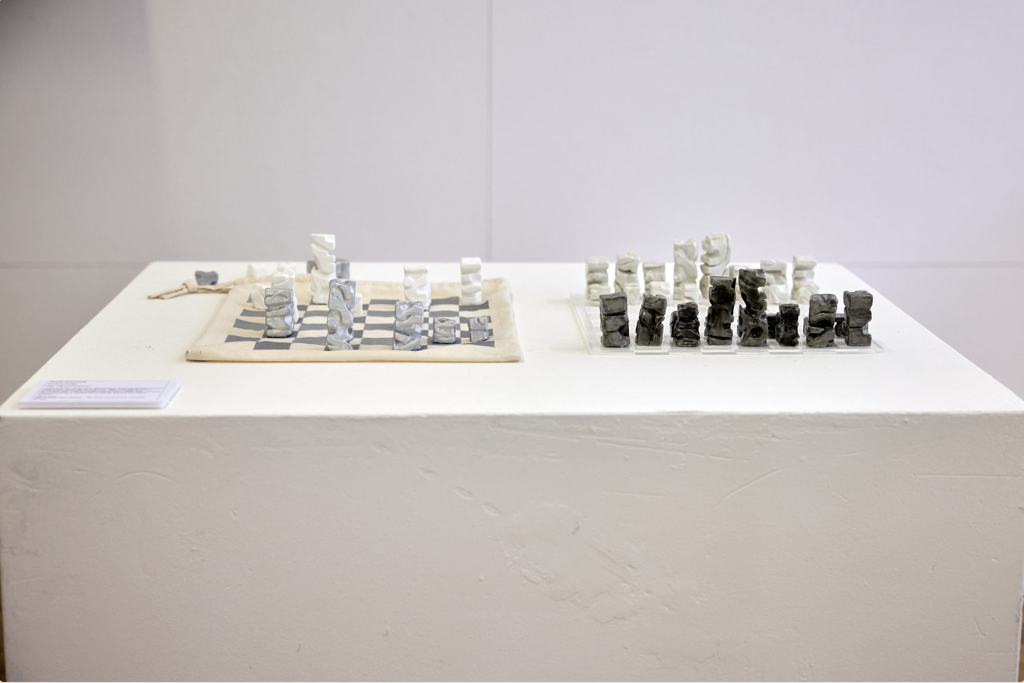 A canvas chessboard and bag with abstract sets of blocks in black, white, light grey and dark grey arranged as chess pieces