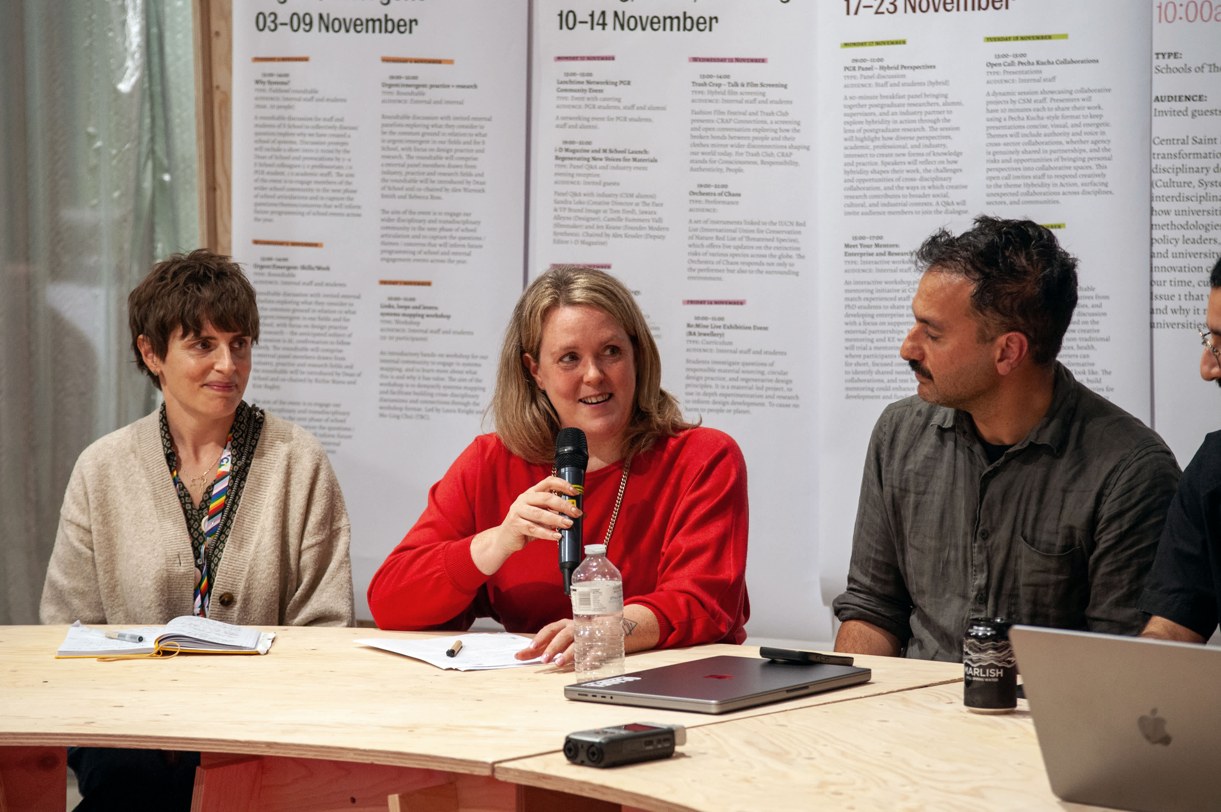 Close-up on a trio of speakers in a panel. The person in the middle is holding a mic and speaking while the others listen.