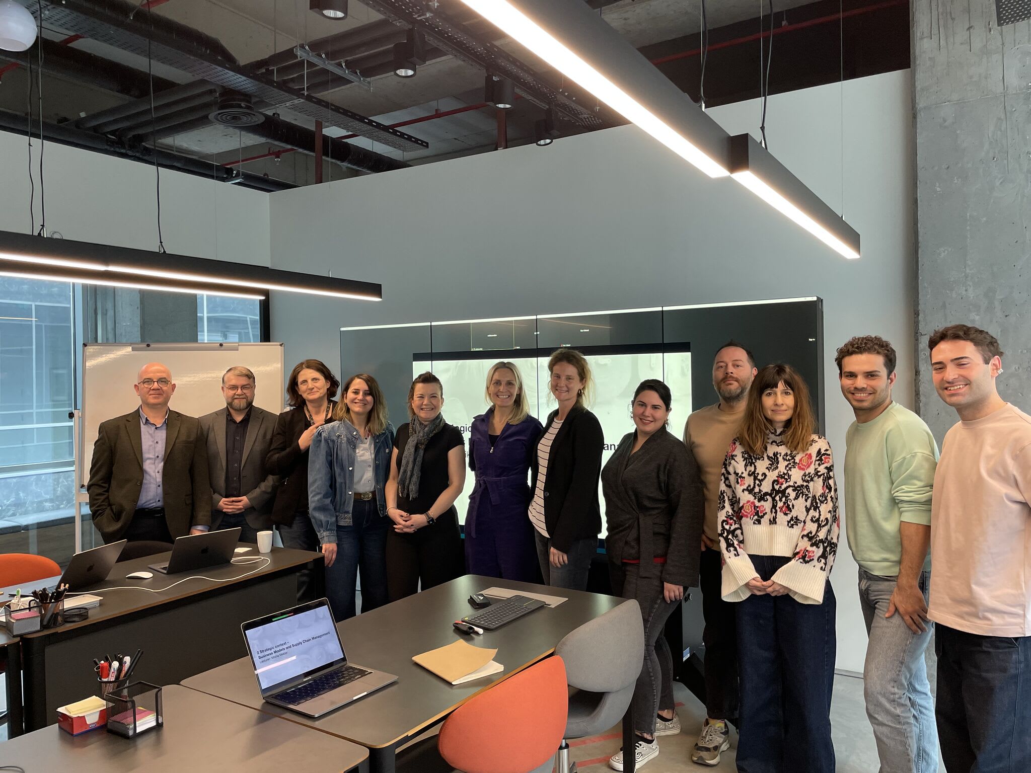 A group shot of 12 individuals standing at the front of a classroom