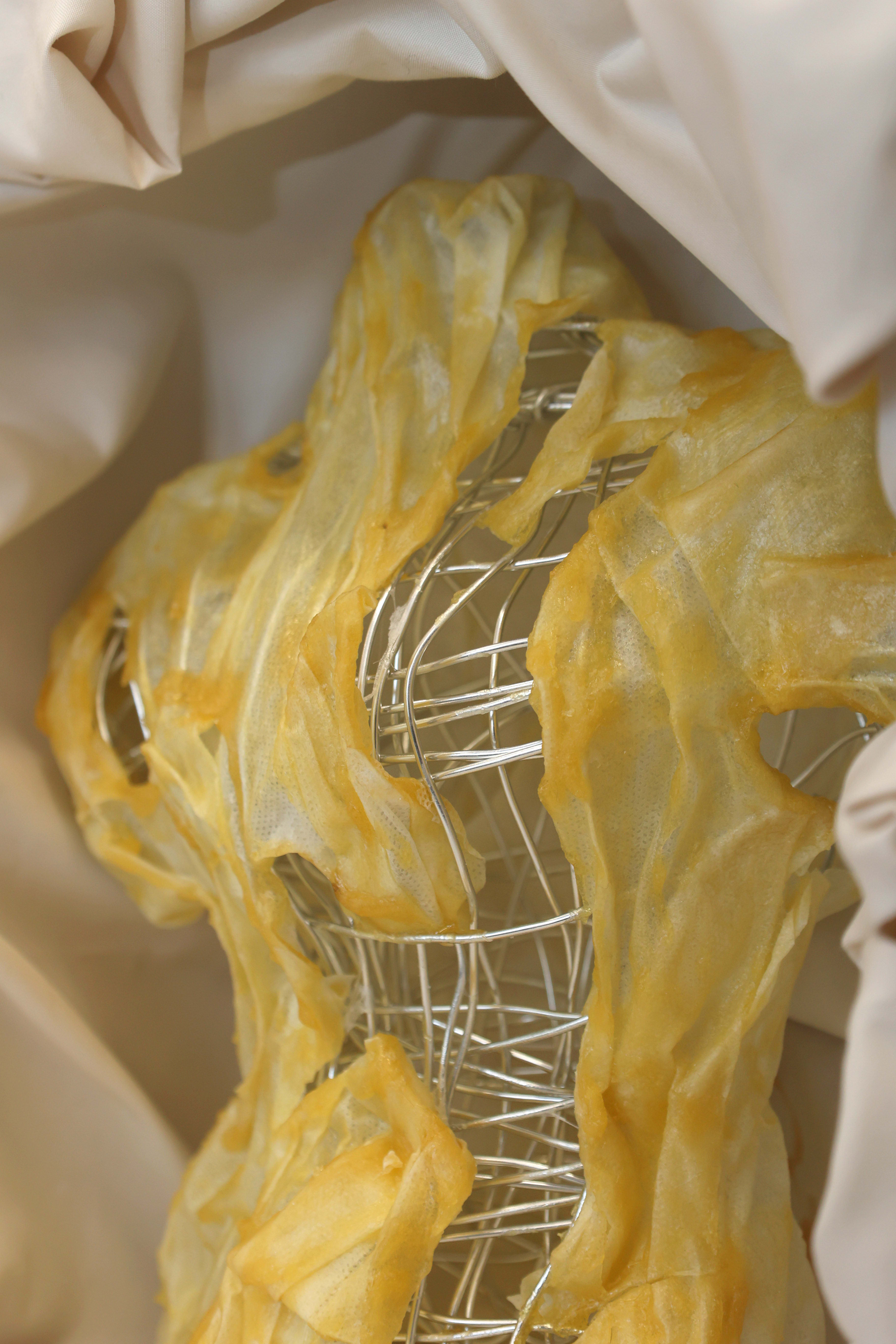 A close up of a sculpture covered with yellow fabric, the sculpture is made with metal wire