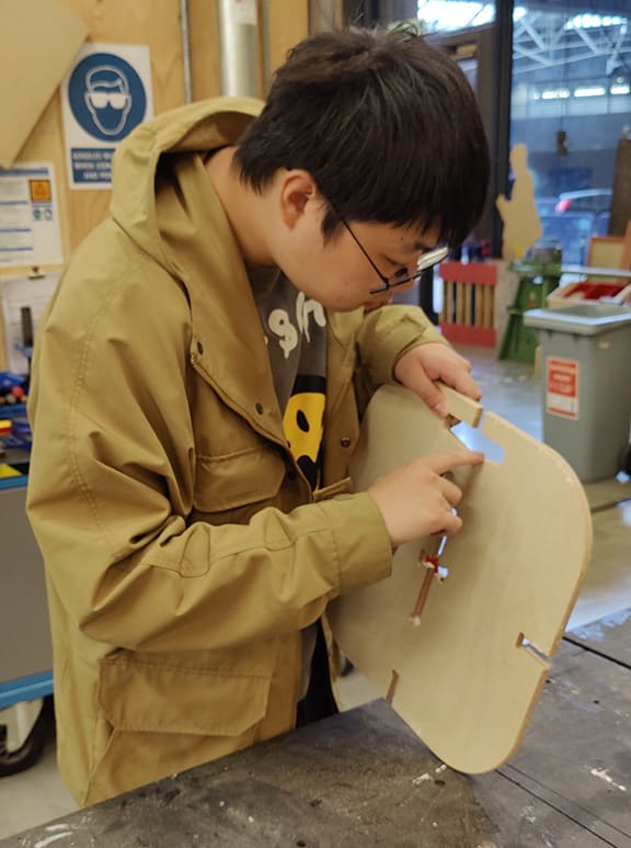 Student carving a wooden furniture prototype.