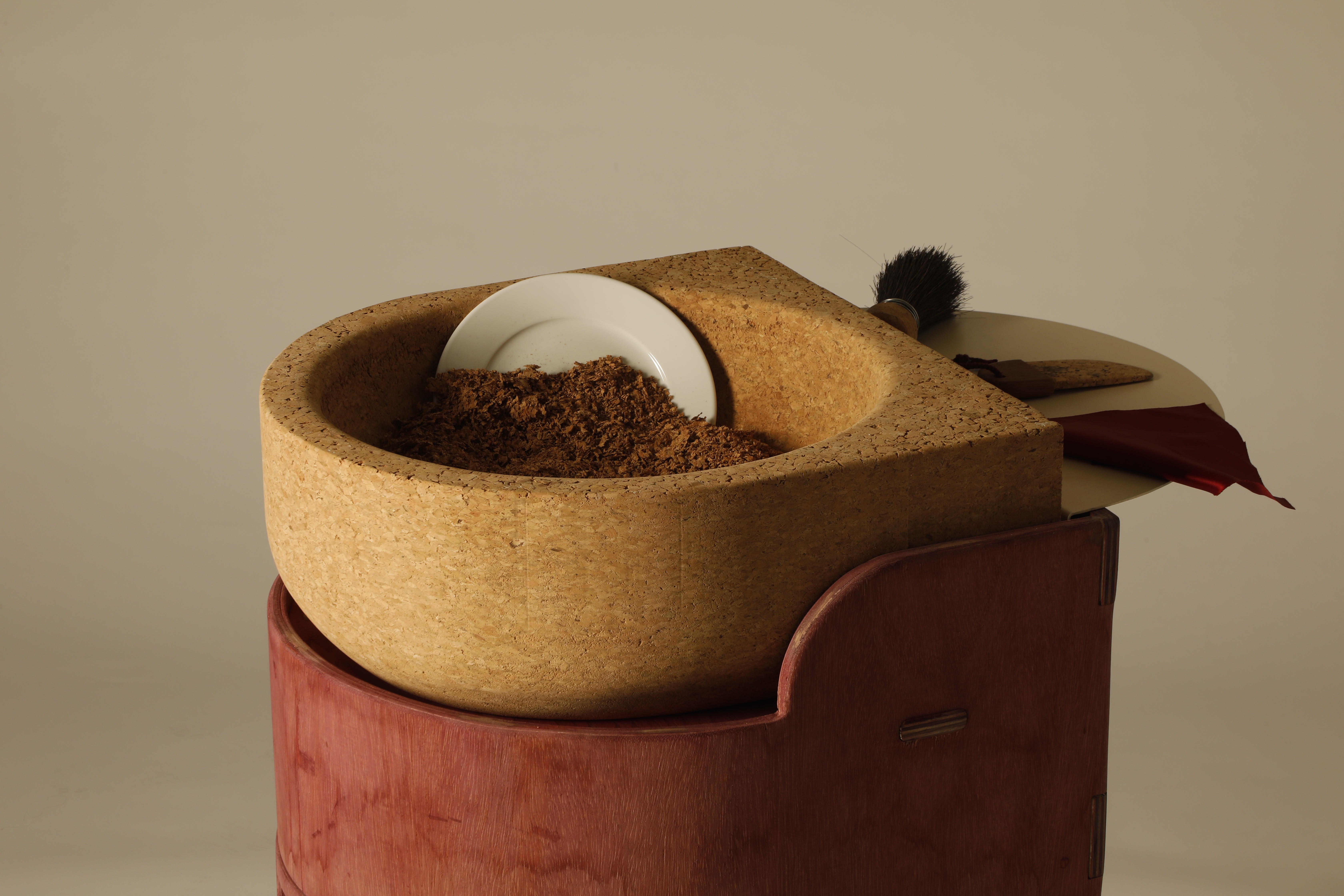 White plate dug into ground in a bowl made out of cork placed on a red wooden table with a brush next to it.
