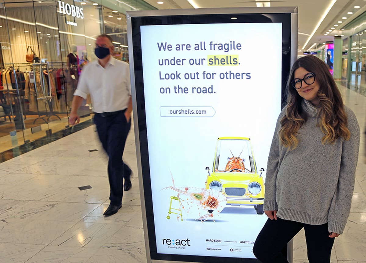 A girl stands in front of a digital advertising board.