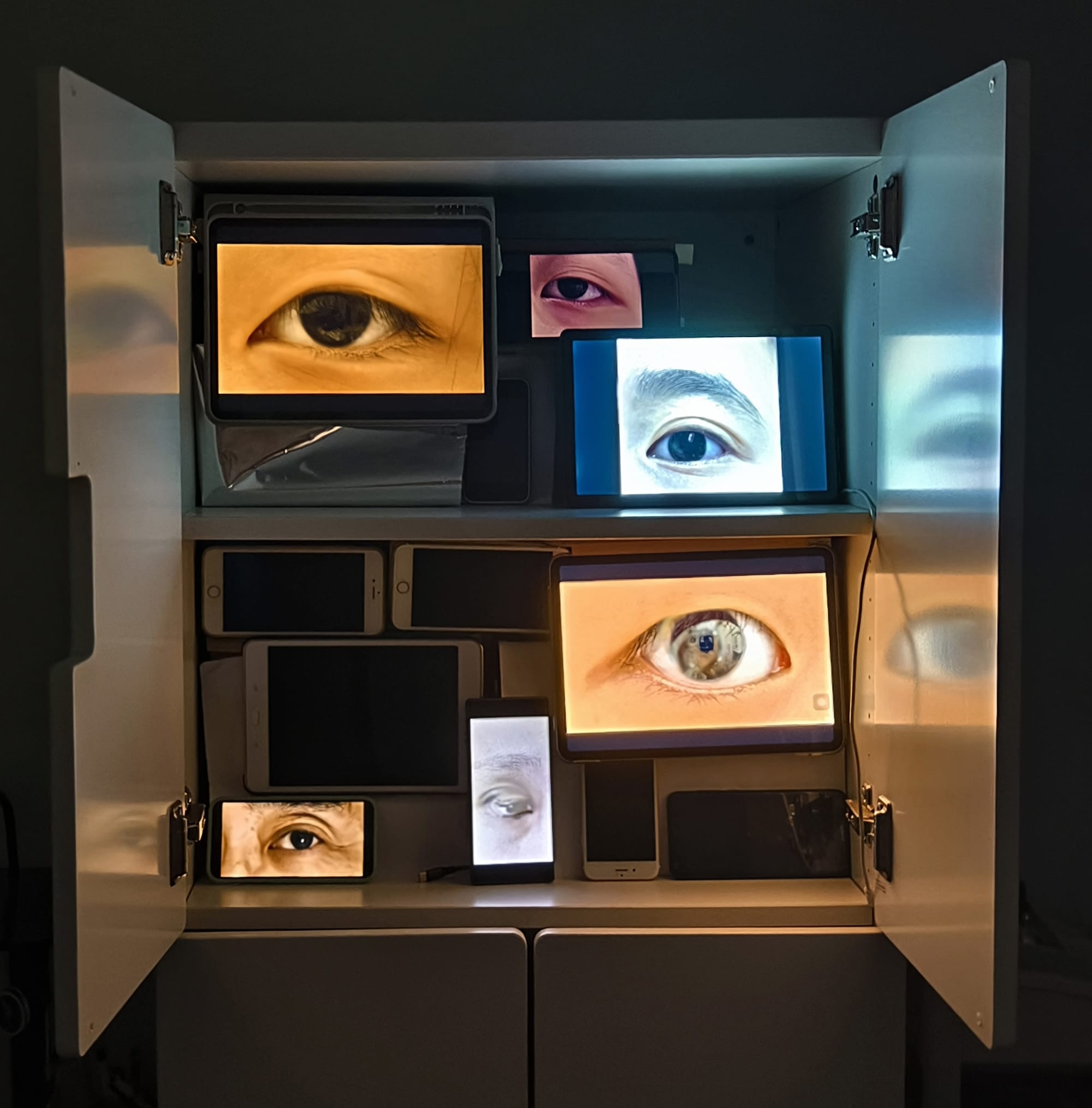 A cabinet is filled with phone and tablet screens showing eyes